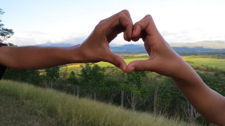 Children make a heart symbol with their hands against the green view from the HIV care program in Honduras run by Montaña de Luz