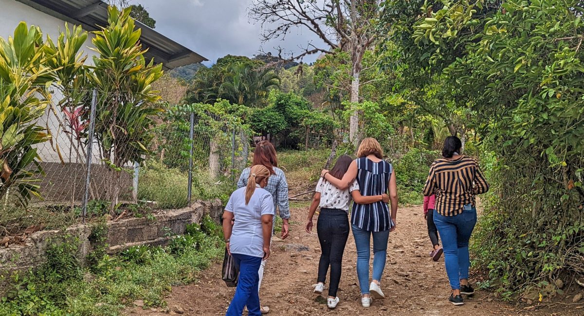 A teen girl from the HIV children's home in Honduras joins staff walking along a dirt path for a visit to her family in a rural area of Honduras